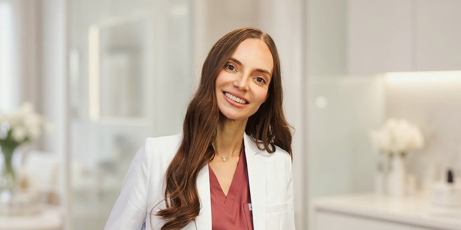 Dr. Maria Shalev in the clinic reception, beside a screen showing the clinic name.